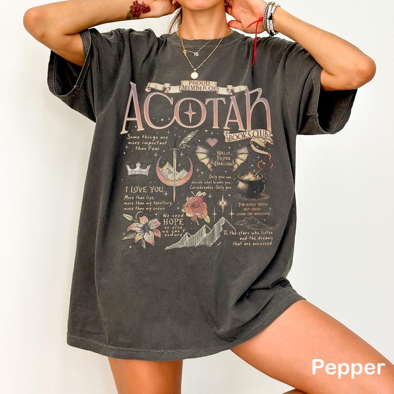 May include: Dark gray t-shirt with the text "ACOTAR BOOKS CLUB" and various graphics, including a crown, sword, and floral elements. The shirt also features quotes and the word "Pepper" at the bottom.