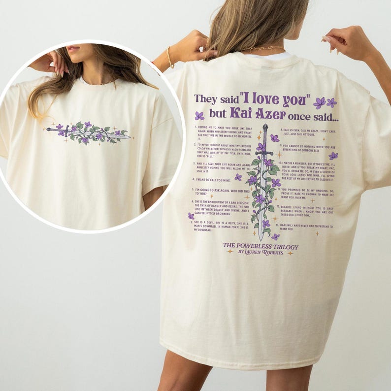 Puede incluir: Camiseta color crema con un dise&ntilde;o floral y de espada en la parte delantera y trasera. La parte trasera presenta el texto "They said 'I love you' but Kai Azer once said..." y una lista de citas. La camiseta es parte de "The Powerless Trilogy" de Lauren Roberts.
