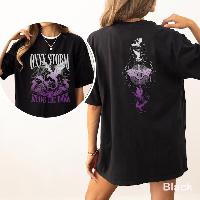 Puede incluir: Camiseta negra con un dise&ntilde;o gr&aacute;fico frontal que presenta un drag&oacute;n, las palabras "ONYX STORM" y "BRAVE THE DARK" en blanco y morado. La parte trasera de la camiseta tiene un dise&ntilde;o de drag&oacute;n a juego en morado y blanco.