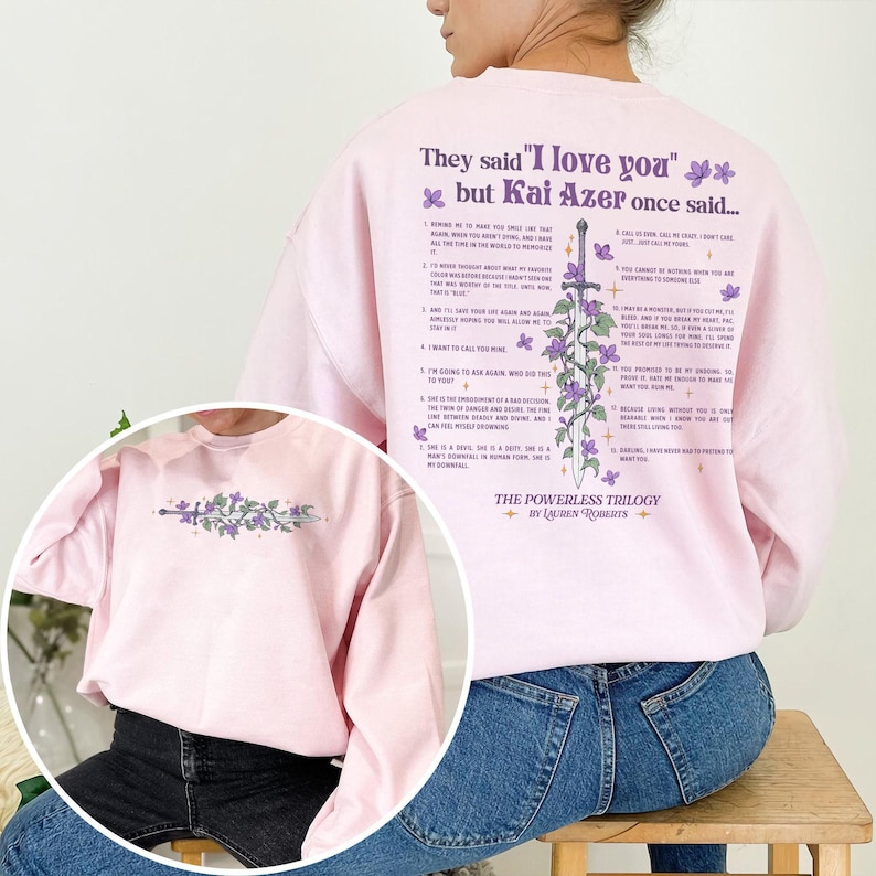 Puede incluir: Una sudadera rosa claro con el texto "They said 'I love you' but Kai Azer once said..." y un dise&ntilde;o de espada con flores moradas. La parte trasera de la sudadera tiene una lista de texto. The Powerless Trilogy by Lauren Roberts.