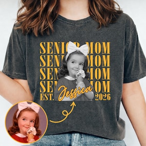 May include: Dark gray t-shirt featuring a vintage black and white photo of a young girl with a bow in her hair, holding an ice cream cone. The shirt has the words "SENIOR MOM" and "Jessica EST. 2026" in yellow.