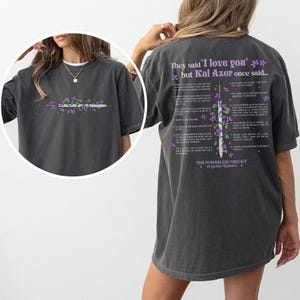 Puede incluir: Camiseta gris oscuro con un dise&ntilde;o floral y de espada en la parte delantera y texto en la parte trasera. El dise&ntilde;o frontal incluye una espada con flores moradas. La parte trasera de la camiseta tiene el texto "They said 'I love you' but Kai Azer once said..." y una lista de citas.