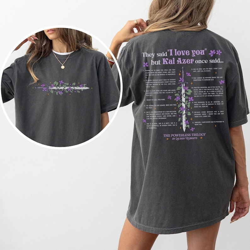 Puede incluir: Camiseta gris oscuro con un dise&ntilde;o floral y de espada en la parte delantera y texto en la parte trasera. El dise&ntilde;o frontal incluye una espada con flores moradas. La parte trasera de la camiseta tiene el texto "They said 'I love you' but Kai Azer once said..." y una lista de citas.