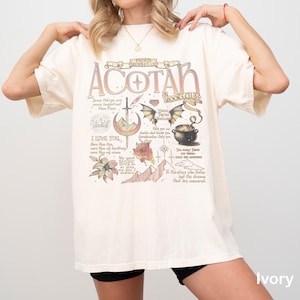 May include: Ivory-colored t-shirt with the text "ACOTAR BOOKS CLUB" in a vintage style. The design includes a sword, wings, a cauldron, and other illustrations. The words "I LOVE YOU" and "We need HOPE" are also visible.