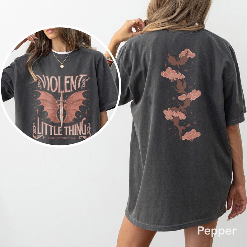 May include: Dark gray t-shirt with the text "VIOLENT LITTLE THING" and a graphic of a sword with wings on the front. The back of the shirt features a design of clouds and bats. The shirt is a Pepper color.