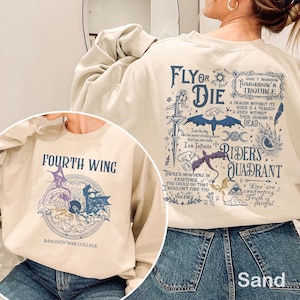 Puede incluir: Sudaderas de color arena con diseños gráficos. Una presenta "FOURTH WING" y una ilustración de dragón, la otra tiene el texto "FLY OR DIE" y "RIDERS QUADRANT" con imágenes de dragones y espadas. Ambas tienen texto adicional.