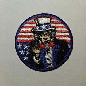Puede incluir: Parche bordado con el Tío Sam haciendo el dedo medio, con un fondo de bandera estadounidense roja, blanca y azul.