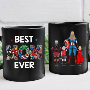Puede incluir: Dos tazas de cer&aacute;mica negras. Una taza tiene el texto "BEST MOM EVER" con un tema de superh&eacute;roes. La otra taza presenta a una madre superhero&iacute;na con tres hijos. Los nombres de los ni&ntilde;os est&aacute;n impresos debajo.