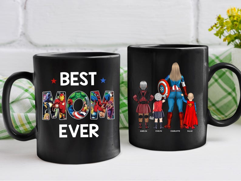 Puede incluir: Dos tazas de cer&aacute;mica negras. Una taza tiene el texto "BEST MOM EVER" con un tema de superh&eacute;roes. La otra taza presenta a una madre superhero&iacute;na con tres hijos. Los nombres de los ni&ntilde;os est&aacute;n impresos debajo.