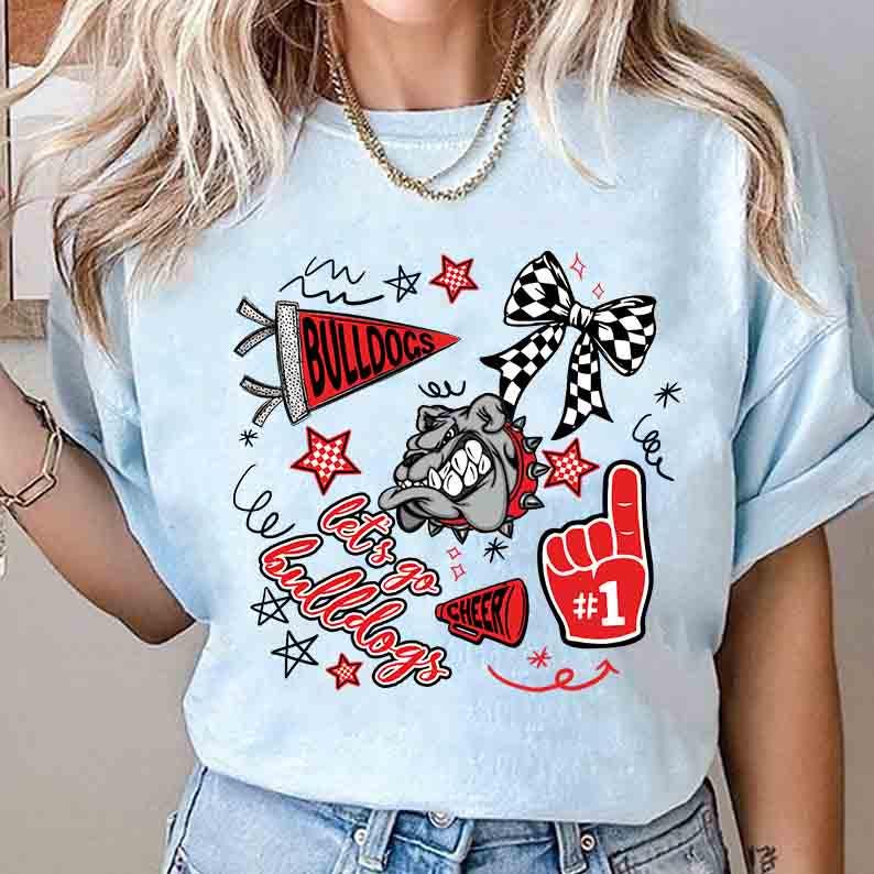 May include: Light blue t-shirt featuring a graphic design with the text "Bulldogs" on a pennant, a bulldog illustration, and the words "Let's go Bulldogs". The design includes red stars, a #1 foam finger, and a black and white checkered bow.