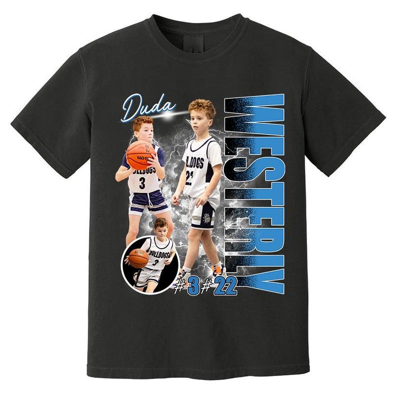 May include: Black t-shirt featuring a basketball player design. The design includes the name "Duda", the word "WESTERLY" in blue, and the numbers "3" and "22". The player is wearing a white and blue basketball uniform and holding a basketball.