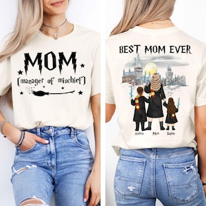 Puede incluir: Camiseta color crema con el texto "MOM (manager of mischief)" y un gráfico de escoba en la parte delantera. La parte trasera de la camiseta presenta una ilustración familiar con el texto "BEST MOM EVER" y nombres.