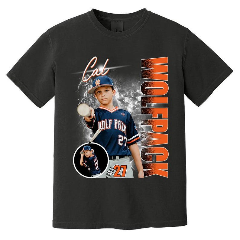 May include: Black t-shirt featuring a baseball player in a navy blue and white uniform with the text "WOLFPACK" in orange. The shirt also includes the name "Cal" and the number "27". A smaller image of the player is in a circle.