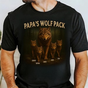 May include: Black t-shirt with a wolf pack illustration. The design shows a large wolf and four smaller wolves, with the text "PAPA'S WOLF PACK" above. Names are printed below the wolves: Tommy, Sophia, David, John, and Eva.