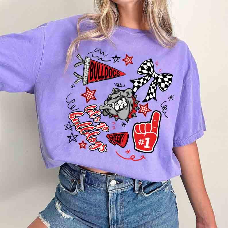 May include: A lilac-colored t-shirt featuring a bulldog graphic and the text "Bulldogs." The design includes a pennant, stars, a checkered bow, and a foam finger with the number one. The words "Let's go Bulldogs" and "Cheer" are also included.