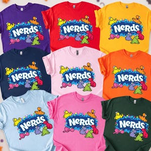 May include: A collection of eight short-sleeved t-shirts in various solid colours including purple, red, yellow, navy, light pink, orange, light blue, bright pink, and dark green, each featuring the Nerds candy logo and colourful character graphics.
