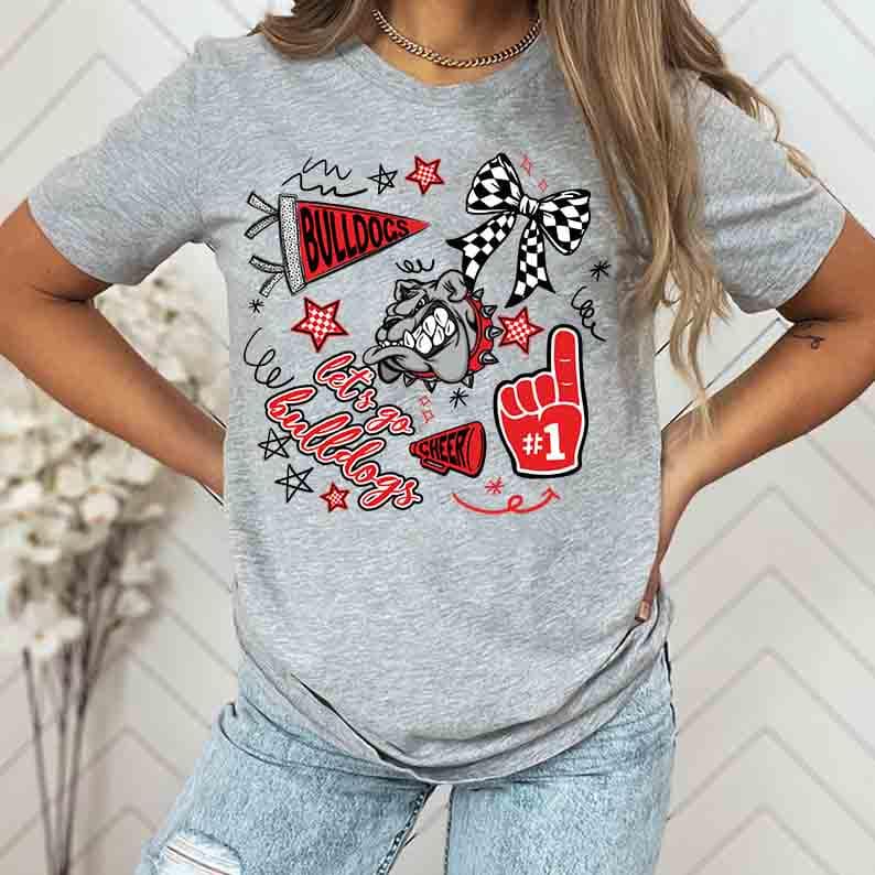 May include: A gray t-shirt featuring a bulldog graphic with the text "Bulldogs", "Let's go Bulldogs", and "Cheer". The design includes a red foam finger, stars, and a checkered bow.
