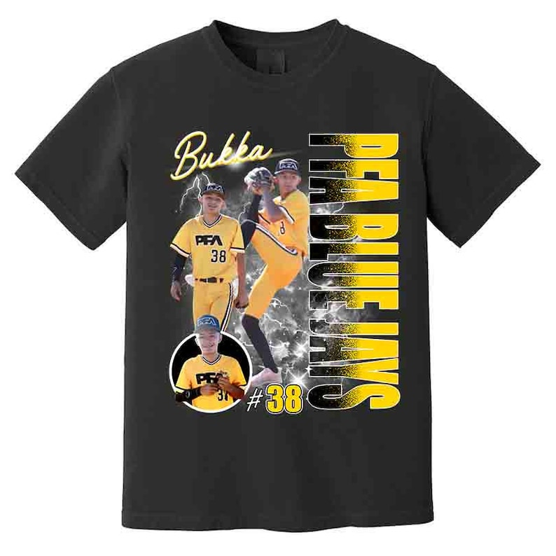 May include: Black t-shirt featuring a baseball player image with the text "Bukka" in yellow script. The shirt also displays "Pea Blue Jays" in vertical yellow letters and the number "38". The design includes a lightning bolt graphic.