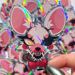 May include: A holographic sticker featuring a cartoon character with pink ears, white fur, and a red bow tie. The character has a menacing expression with sharp teeth and one eye covered by a black patch. The sticker has a glittery, iridescent finish.