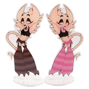 May include: Two acrylic standees featuring a cartoon character with a light tan complexion, large ears, and a mischievous expression. One standee has brown striped legs, the other has pink striped legs. Both have black tops and are on clear bases.