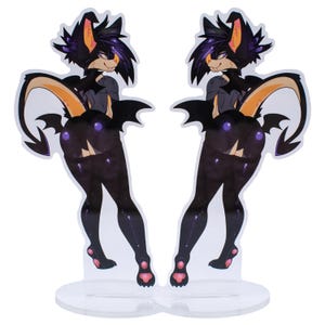 May include: Two acrylic standees featuring a stylized black and purple creature with bat-like wings and a tail. The creature has a furry appearance with orange and purple accents. The standees are on clear, circular bases.