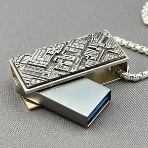 May include: A silver necklace with a textured rectangular pendant that opens to reveal a silver USB drive. The chain is a silver box chain.