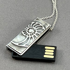 May include: A silver necklace with a silver pendant that opens to reveal a black USB drive. The pendant features an intricate design of a nautilus shell.