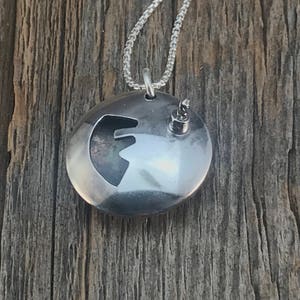 May include: A silver pendant necklace with a round disc charm featuring a cut-out design of a stylized letter F. The pendant is hanging on a silver chain.