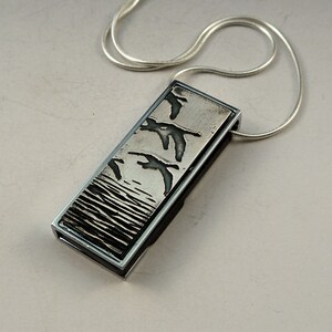 May include: A silver pendant necklace with a rectangular silver charm featuring an etched design of birds flying over water.