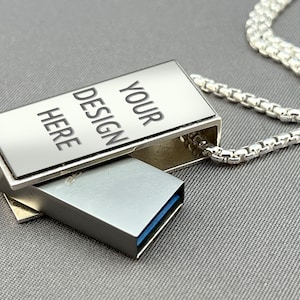 May include: A silver metal USB drive with a chain attached. The drive has a sliding cover that reveals the USB port. The cover is engraved with the text "YOUR DESIGN HERE".