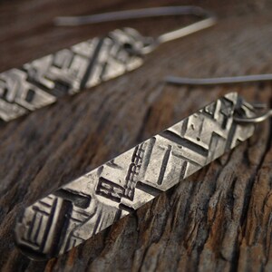 May include: A pair of silver earrings with a geometric pattern. The earrings are made of metal and have a hook closure.