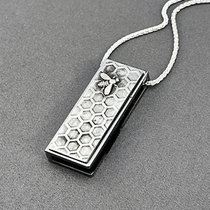 May include: A silver necklace with a rectangular pendant featuring a honeycomb pattern and a small bee charm.