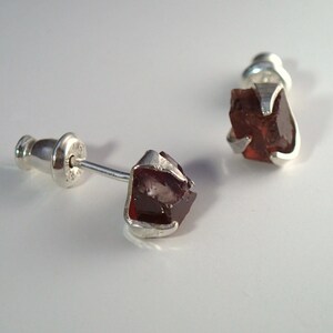 May include: A pair of silver stud earrings with a dark red, faceted gemstone in each setting.