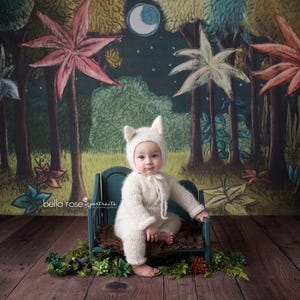 May include: A baby wearing a white knitted onesie with a white knitted cat hat sits on a green wooden bench. The background is a whimsical forest scene with trees, leaves, and a crescent moon.