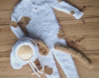 May include: White and brown fuzzy knitted baby outfit with a matching hat. The outfit has a long tail and brown spots.