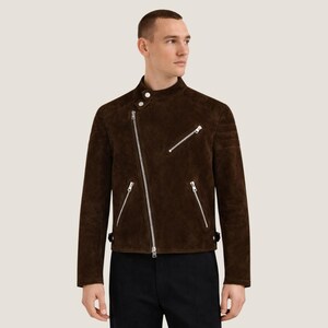 May include: A brown suede jacket with an asymmetrical zipper closure and multiple silver zippers. The jacket has a stand-up collar and a tailored fit. The sleeves are long, and the jacket appears to be made of a soft, high-quality material.