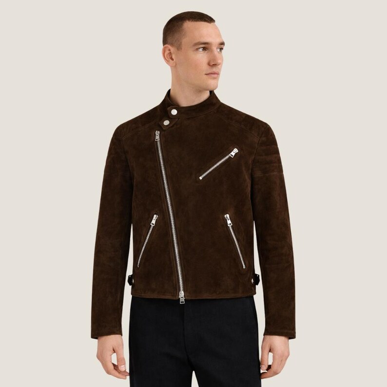 May include: A brown suede jacket with an asymmetrical zipper closure and multiple silver zippers. The jacket has a stand-up collar and a tailored fit. The sleeves are long, and the jacket appears to be made of a soft, high-quality material.