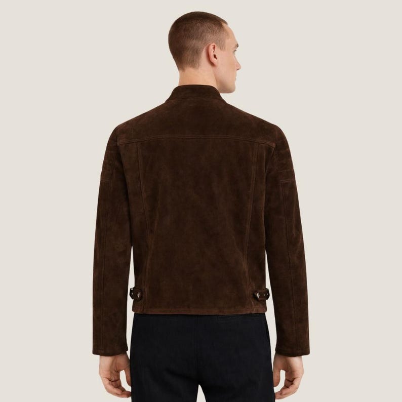 May include: A brown suede jacket with a stand-up collar and long sleeves. The jacket has two small pockets on the chest and two adjustable buckles at the waist. The jacket is a rich, dark brown color.