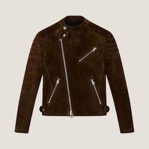 May include: A brown suede jacket with a classic biker style. The jacket features a diagonal zipper, multiple zippered pockets, and a snap-closure collar. The jacket has a textured appearance and a tailored fit.
