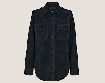 Peut inclure: Une chemise en daim noir à manches longues, deux poches poitrine et un col chemise. La chemise a des épaulettes et une fermeture boutonnée sur le devant. Le tissu semble doux et texturé, avec un aspect légèrement usé.