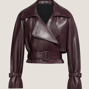 May include: A burgundy leather jacket with a wide collar, a wrap-style front, and a matching belt. The jacket features long sleeves with buckle details at the cuffs. The overall design is sleek and modern, suitable for various occasions.