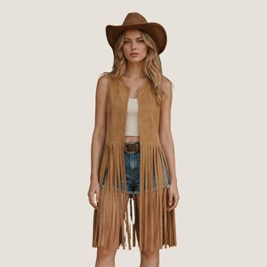 May include: A tan suede vest with long fringe detailing. The vest is worn with a brown belt, denim shorts, and a brown cowboy hat. The outfit has a bohemian, western aesthetic.