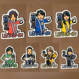 May include: A set of seven die-cut stickers featuring illustrated characters in various coloured uniforms, each holding a handheld device. The text "LET'S GO-ON" is printed in bold letters at the bottom of each sticker, which have a holographic finish.