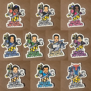 May include: A collection of nine die-cut stickers featuring illustrated characters in superhero-style uniforms with yellow and black chevron patterns. Each character holds a weapon and displays the text UNLEASH THE POWER in various colors.