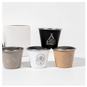 May include: Five stainless steel shot glasses in black, white, tan, and grey. Each glass has a different outdoor-themed design, including a tent, motorcycle, and bear paw prints. The glasses have a silver rim.
