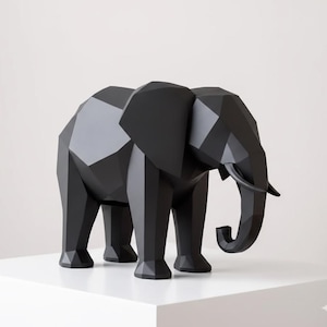Könnte beinhalten: Eine schwarze geometrische Elefantenskulptur mit polygonalem Design. Der Elefant hat große Ohren, einen Rüssel und Stoßzähne. Die Skulptur wird auf einer weißen Oberfläche vor weißem Hintergrund ausgestellt. Es ist ein modernes Wohnaccessoire.
