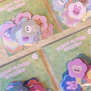 May include: Four packs of SKZOO Flower Stickers, each containing 32 units. The stickers feature flower-shaped designs with cartoon animal faces in pastel colors. The packaging is green with white text.