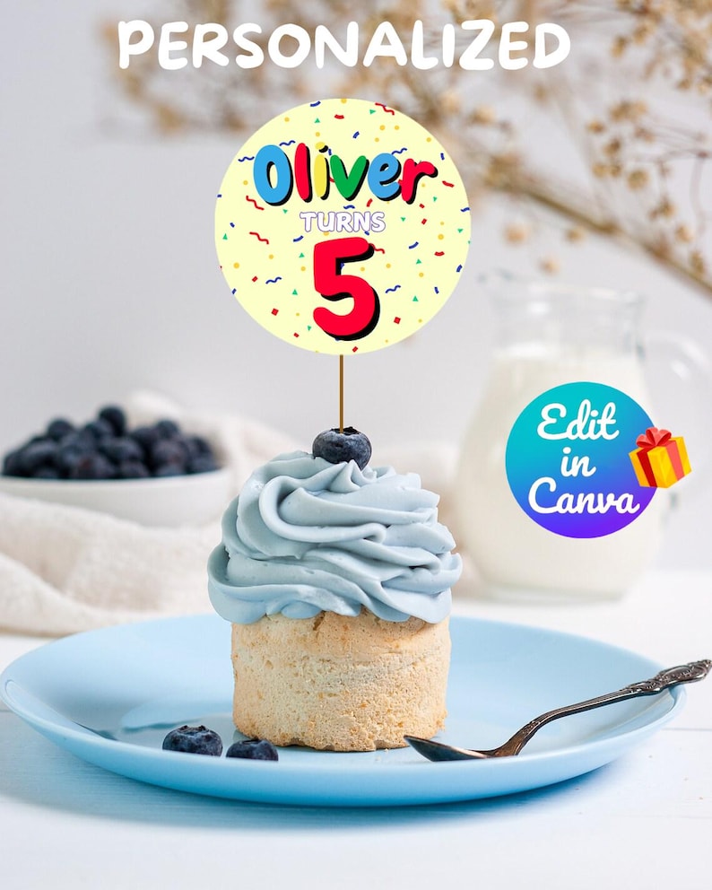 May include: A blue cupcake with white frosting and a single blueberry on top. A yellow and white circular cake topper with the text "Oliver turns 5" in colorful letters.