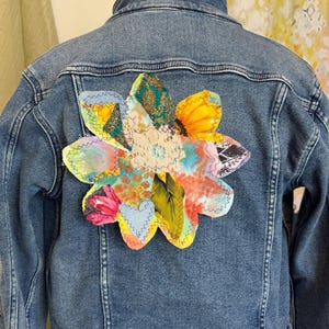 Peut inclure: Une veste en jean bleue avec un motif de fleur en patchwork coloré au dos.