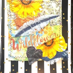 May include: A fabric collage with sunflowers, denim, and lace, and the word "Wildflower". A grey heart is stitched on the collage. The background is black and white stripes with gold polka dots.